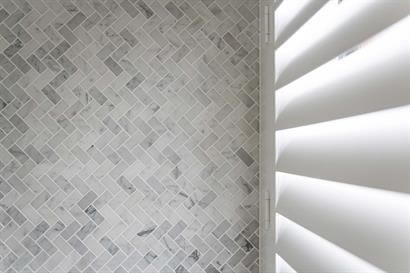 Bathroom wall tiles in classic herringbone pattern against white plantation shutter