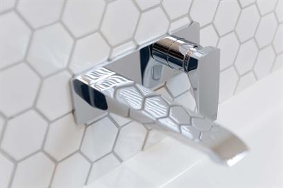 Modern tap and mixer set wall-mounted over bath against classic white hexagonal wall tiles