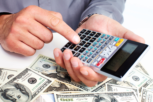 man using calculator at desk with piles of money