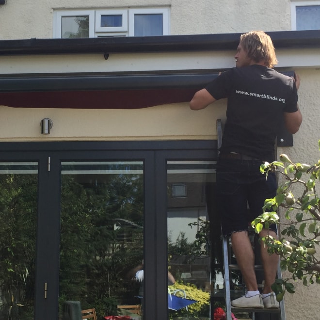 Smart Blinds fitter on a ladder fitting an awning above patio doors