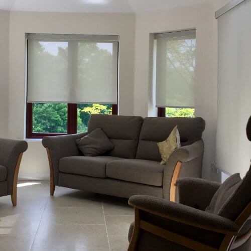 Cream roller blinds in a bay window above a sofa