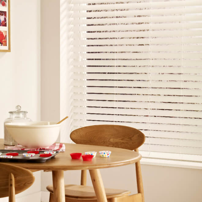 White faux wood Venetian blind with tapes over a dining table