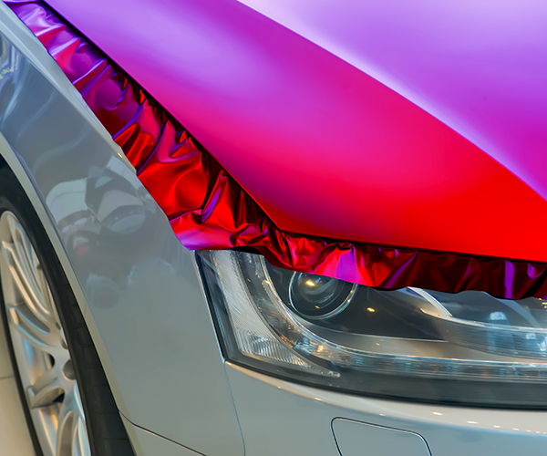 brightly colored vinyl car wrap being applied to the hood of the car