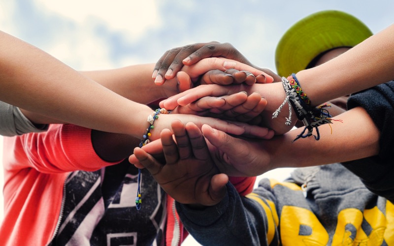 a diverse group of teenagers joining hands together in cooperation