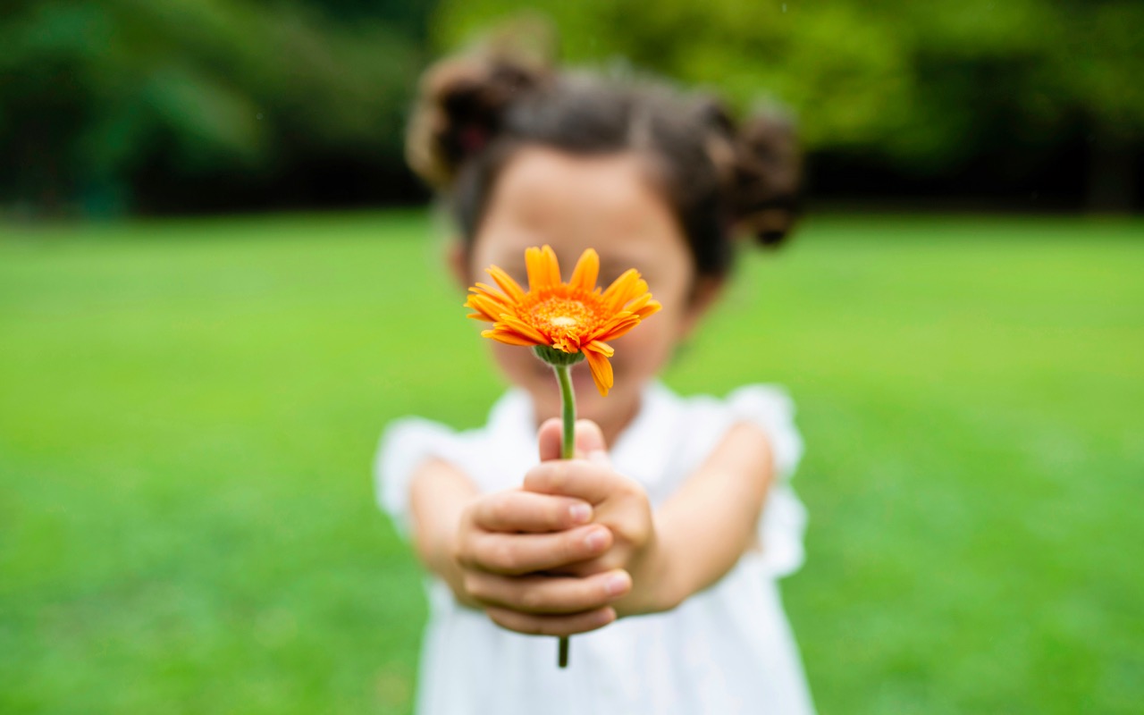 little girl holding up an orange flower