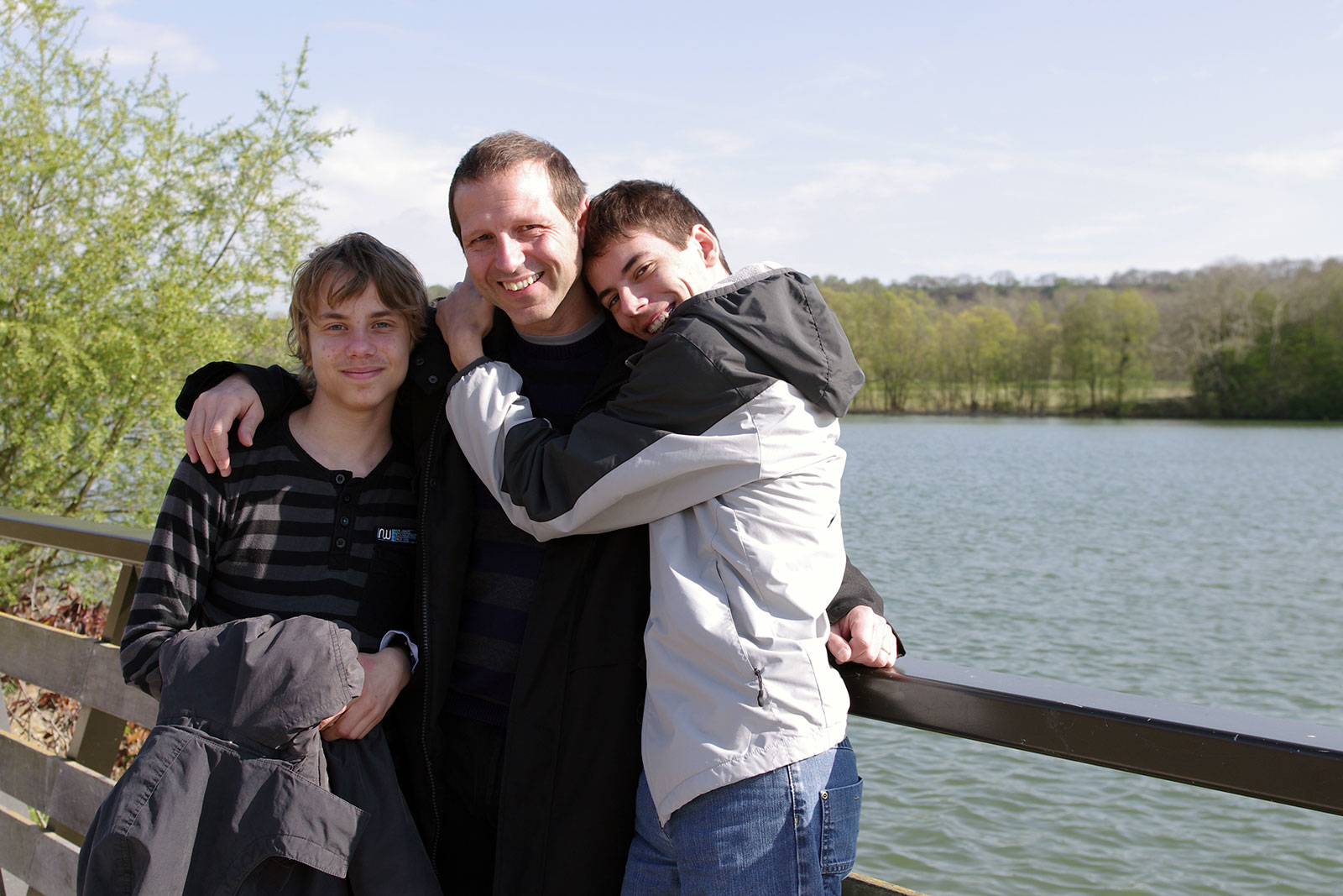 A smiling father with his arm around his two sons on a bridge in a park