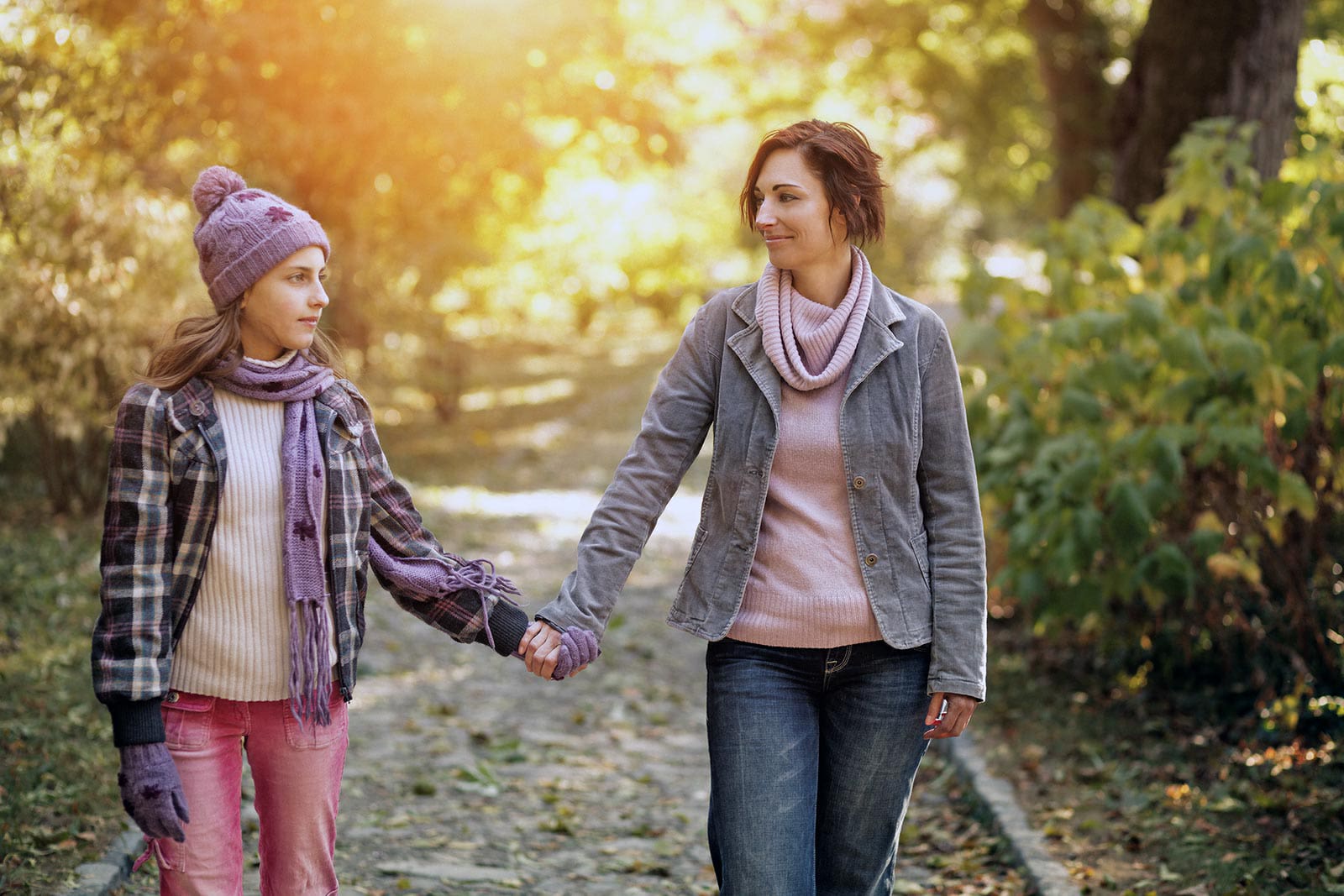 A mom and her teen daughter holding hands together on a walk