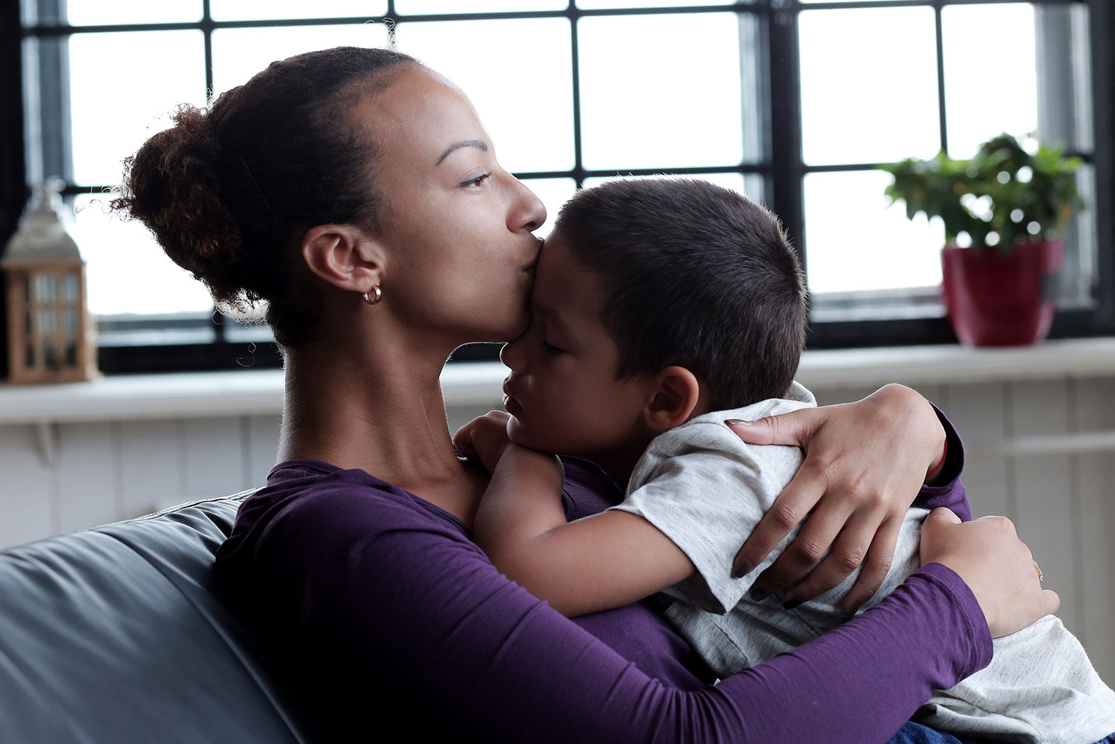 Seated mother embraces her son while kissing him on his forehead