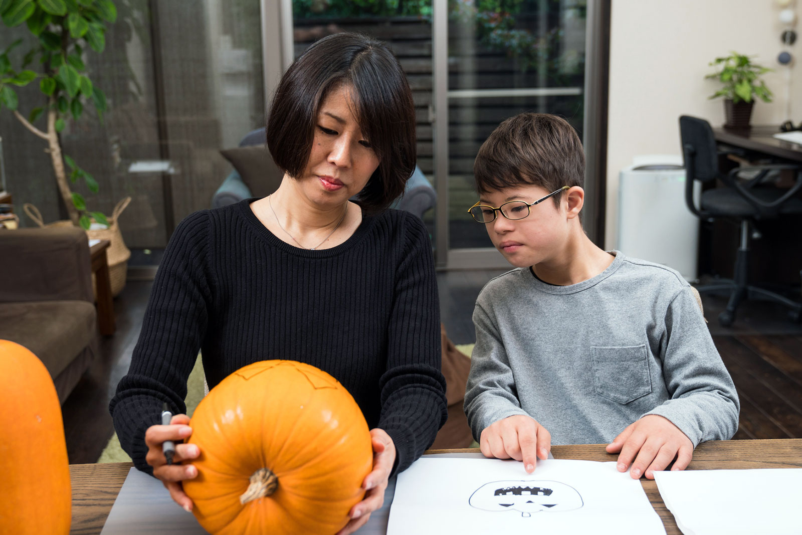 Asian mother helping disabled son prepare a pumpkin for carving