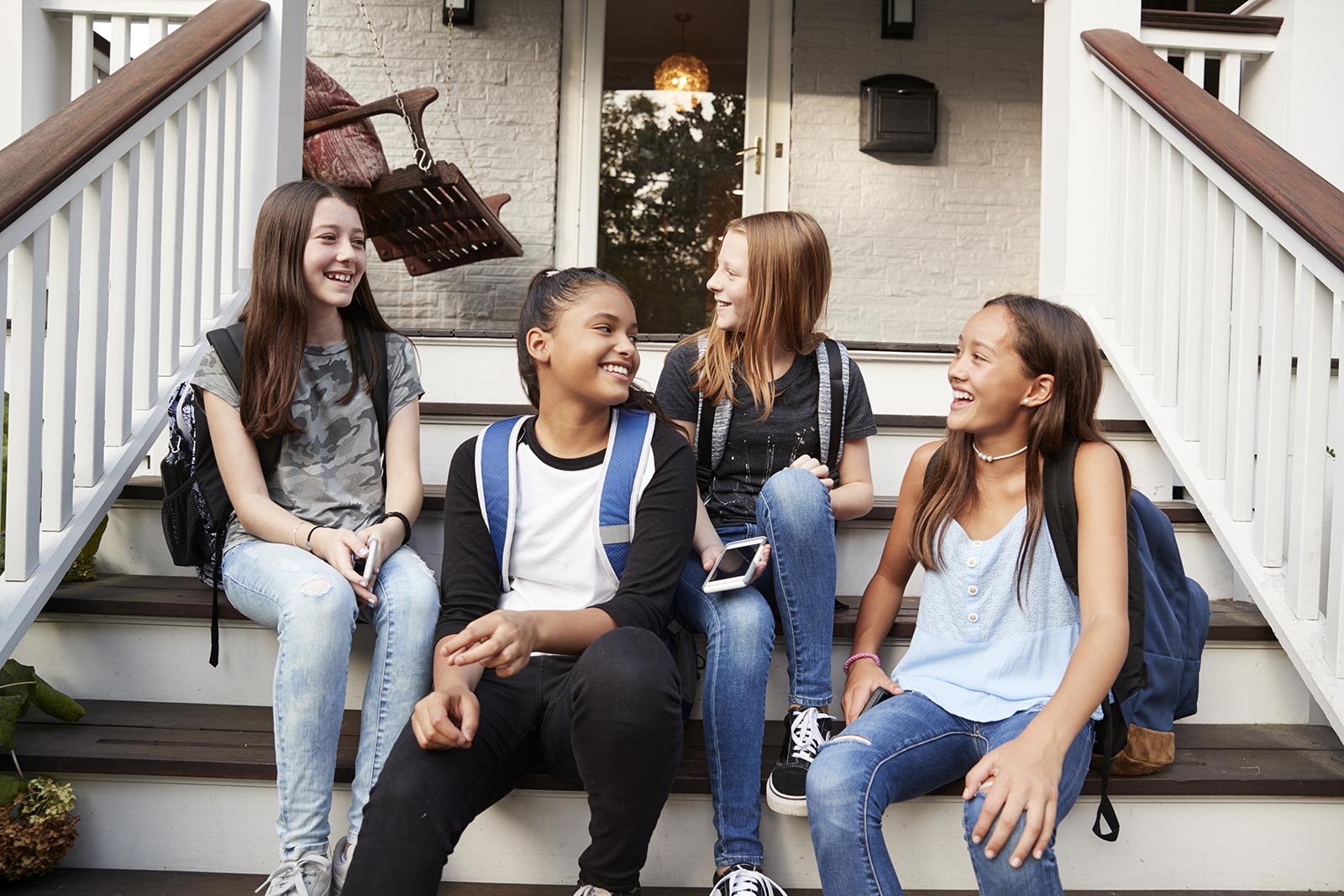 A group of 4 teenage girls chatting on the front steps of a house after school