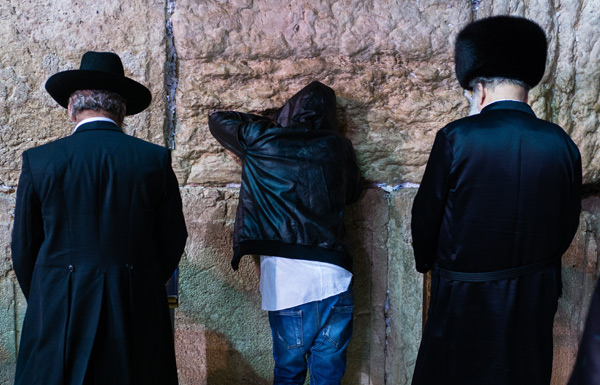 Three people praying on Wailing Wall