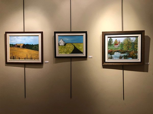 three landscape paintings hanging on gallery wall
