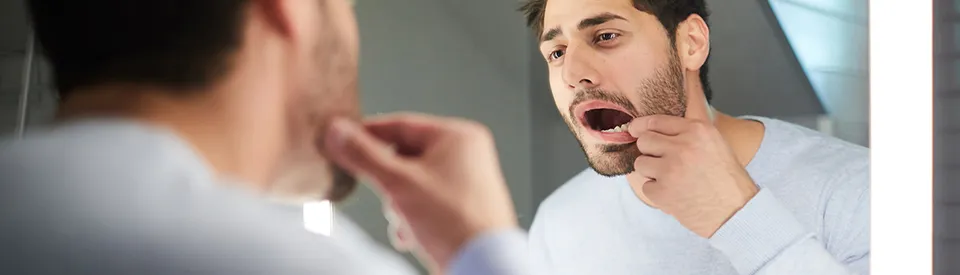 man looking at his teeth in the mirror