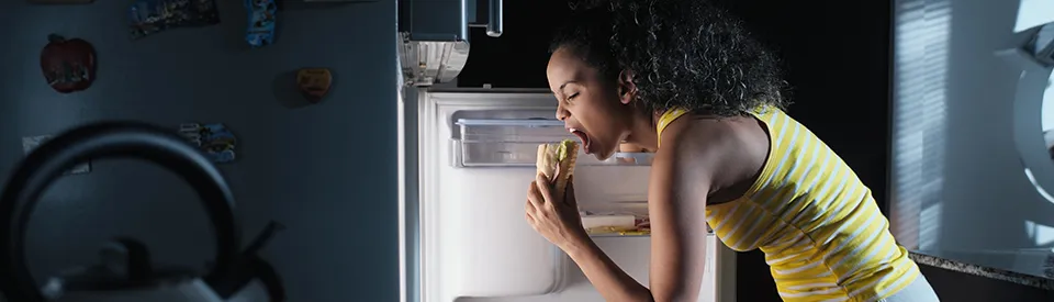 woman snacking while looking in refrigerator