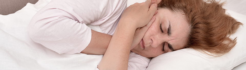 Mature woman with toothache lying in bed and holding her cheek