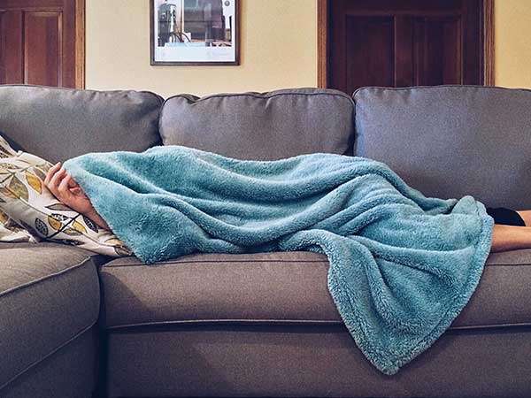 Sick person lying under blanket on couch
