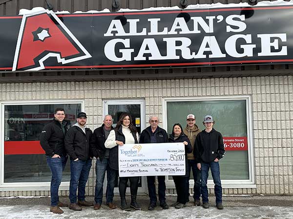 Thompson family pose with donation cheque in front of Allen's Garage.