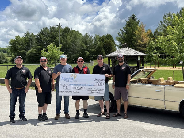 Kinsmen pose with donation cheque in front of 1986 Dodge 600 Convertible