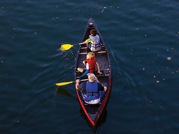 Man and two kids in canoe wearing lifejackets.